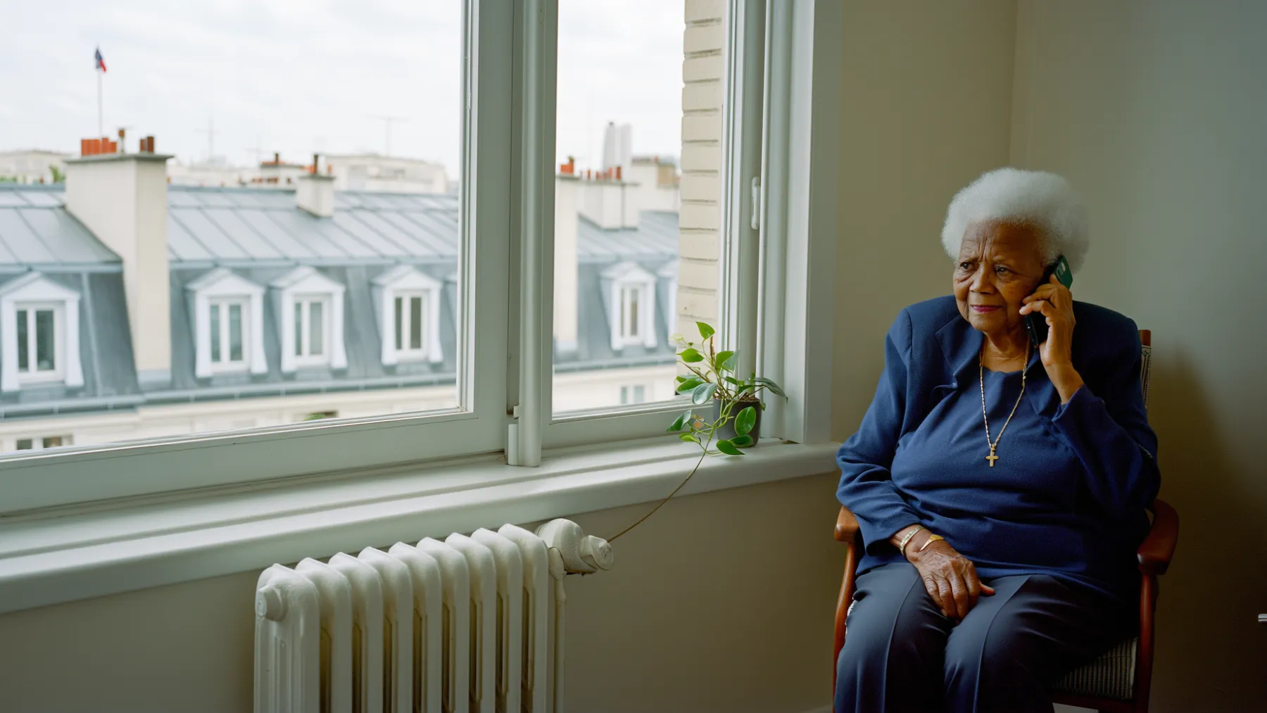 An older woman on the phone by the window of her apartment above city rooftops