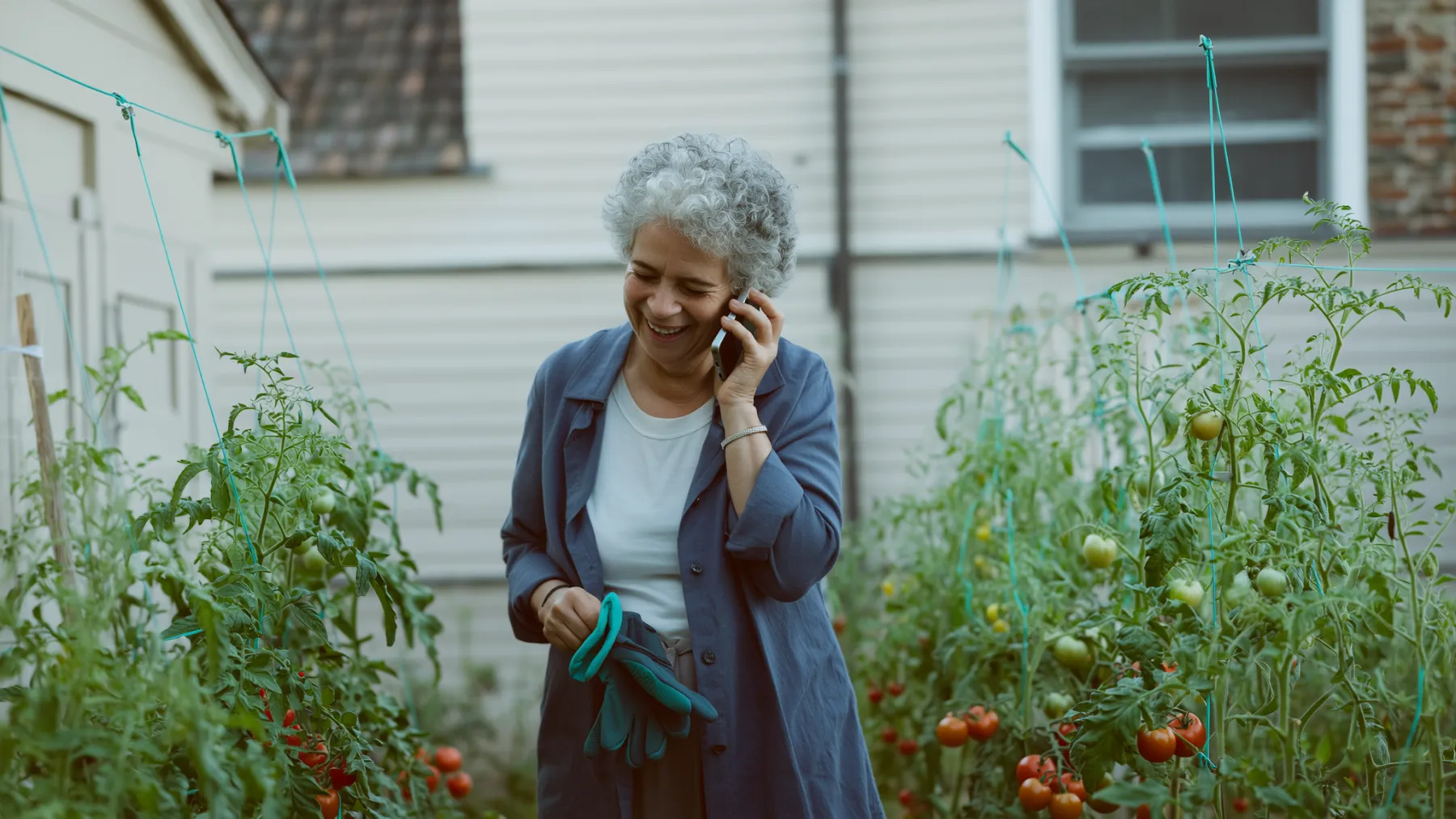 A woman in her sixties laughing on the phone in her vegetable garden
