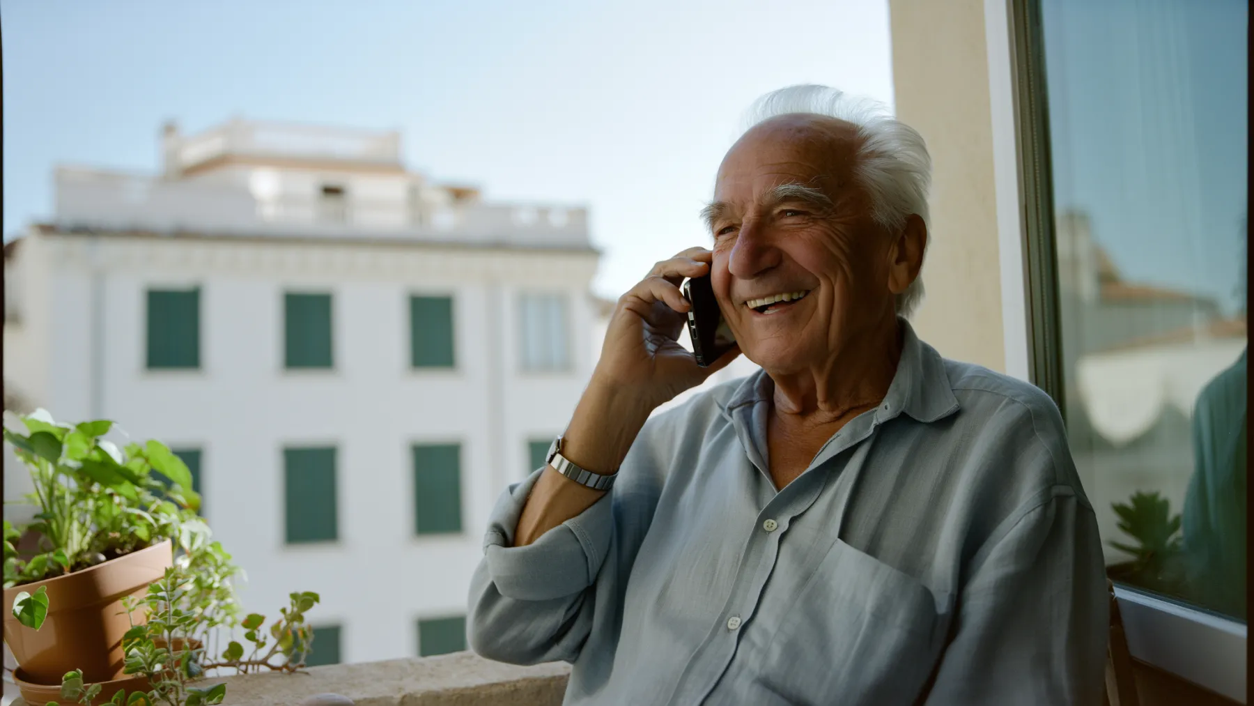 A smiling older man on the phone on a sunny Mediterranean balcony